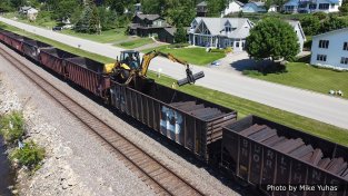 On June 2, 2021, the work train showed up with the tie distribution crew. That’s a fairly standard backhoe with tricked-out outriggers and a bracket on the front bucket to allow it to rest (and be moved upon) the top chords of the tie hoppers. The excavator is equipped with a grapple instead of the typical digging bucket.