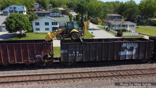 On June 2, 2021, the work train showed up with the tie distribution crew. That’s a fairly standard backhoe with tricked-out outriggers and a bracket on the front bucket to allow it to rest (and be moved upon) the top chords of the tie hoppers. The excavator is equipped with a grapple instead of the typical digging bucket.