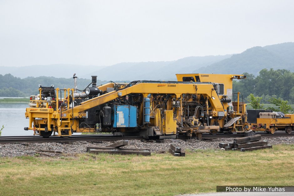 This is a multi-purpose tie aligning machine. The first unit, near the center of the machine (obscured by shrouding), is a ballast broom. If any fine tuning of the tie placement is necessary, the second unit on this machine accomplishes that. Finally, a rotating broom brushes any ballast off the tie ends.