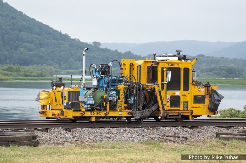 The spiker fastens the tie to the rail. Spike drivers are generally equipped with mechanical arms to shift the rail into proper gage and hold it when inserting the spikes.